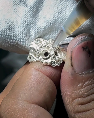 Artisan hand-finishing a floral sterling silver jewelry piece to define oxidized lines and natural texture.